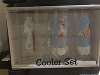 Set of three acrylic or glass drinking glasses in original box with drawings on the surface featuring women and beach themes.