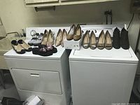 Lot of six pairs of women's shoes displayed on top of laundry machines showing various styles including woven mules, embroidered flats, high heels, peep-toe heels, and ankle boots.