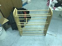 Wooden shoe organizer stand with six horizontal rods and two vertical side panels, placed on a floor.