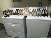 Photo showing eight pairs of new women's high heel shoes in sizes 11 to 12 arranged on top of two white appliances.