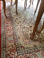 Close-up image showing the intricate floral and vine pattern and the color scheme of the carpet under a dining table.