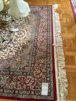 Full view of carpet showing red floral border, cream center field with floral/scroll patterns, and fringe along edge.