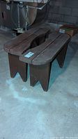 Pair of brown painted wooden benches with contoured seats and angled legs, showing paint wear and some damage on or near feet.