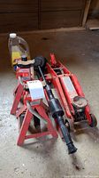 Photo of red hydraulic trolley jack, axle stands, bottles of motor oil and wash and wax, and car wash brush on concrete floor.