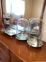 Photo of two large glass cloches with mirrored bases and footed mirrored vanity tray placed on wooden dresser.