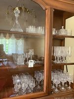 Full view of cabinet shelf showing 2 decanters, tumblers, wine glasses, champagnes flutes, cream and sugar set.