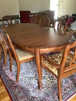 Dining table with four armless chairs around it, showing wood finish and chair upholstery.