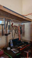 Wide shot showing workbench and wall with hand tools including hammers, saws, level, pliers, and socket set box.
