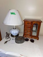 Photo showing 15-inch glass base lamp with white pleated shade, metal trinket box, wooden jewelry box, and sunglasses on a white surface