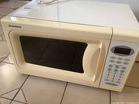 Front and top view of the off-white Sylvania microwave oven with windowed door and control panel.