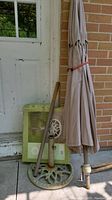 Photo showing cast iron umbrella stand with umbrella folded and strapped, placed beside a door with box behind.