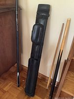 Three pool cues and black carrying case leaning against wall and cabinet