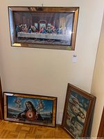 Three religious framed prints hanging and leaning against a wall, including The Last Supper and Virgin Mary images.