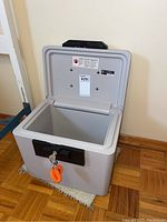 Front and open interior view of the light gray Sentry safe with black handle and key in lock.