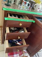 Three wooden kitchen drawers partially open showing contents and folded tea towels