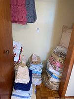 Closet view showing stacks of folded linens including towels, blankets, and sheets on floor and shelves.
