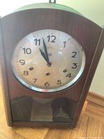 Front view of the Reguladora wall clock in wooden case showing its round dial with numbers and three winding holes.