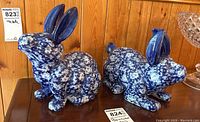Two flow blue ceramic bunny figurines side by side on a wooden surface showing their overall size and shape.
