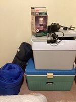 Full lot with coolers stacked, lantern box on top, sleeping bag and air mattress rolled and leaning.