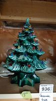 Front view of green ceramic Christmas tree with multi-colored bulbs and textured glaze, showing shape and size relative to the shelf.