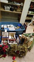 Photo showing plastic bin with assorted Christmas items including wreaths, an angel wall hanging, and red apple ornament.