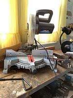 Full side view of Delta 10 inch compound mitre saw on a wooden workbench with a clamp and hand handle visible.