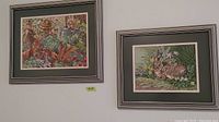 Two framed cross stitch artworks hanging on a wall, one with an autumnal theme and the other with two bunnies in a floral setting