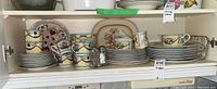 Full view of multiple dish sets including cups, saucers, plates, and serving pieces arranged on shelves.