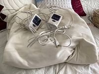 Wide view of the electric blanket with two attached remote controls and cords laid out on a bed.