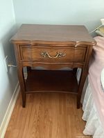 Front angle view of one Malcolm wooden end table showing drawer with brass handle and lower shelf