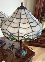 Full view of stained glass table lamp showing scalloped cream-colored shade with colored floral accents and ornate bronze-tone composite base.