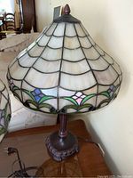 Full view of stained glass lamp with scalloped white glass shades and floral border, ornate dark composite base visible