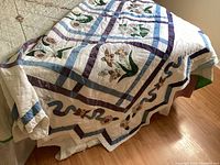 Angle showing quilt draped over bed showcasing patchwork squares and floral appliqué design with scalloped edge.