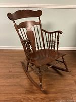Front angle showing full wooden rocking chair with curved seat and armrests, visible scratches on wood surface.