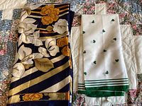 Photo displaying two scarves: a dark navy floral patterned scarf and a white scarf with green shamrock motif and border stripes on a quilted background.