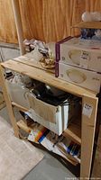 Wooden shelf shown against unfinished wall with cardboard boxes and light fixtures on top and inside.