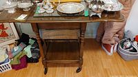 Straight-on view of the wooden tea cart showing the folding side tray on the left, lower shelf, turned legs and casters.
