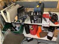 Overall view of two shelves containing various power tools, hand tools, automotive supplies, and painting supplies. Items include jerry can, car mats, painting supplies, and boxed items.
