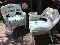 Two white wicker armchairs with blue and green striped cushions and a small white wicker table on outdoor deck.