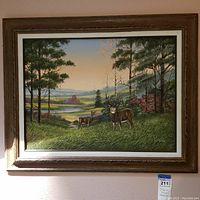 Front view of framed painting featuring two deer in a forest landscape with distant hills and water, showing signature and ornate frame.