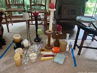 View of various candles and candle holders arranged on carpet, including tall white wooden candle holder and black wrought iron stand