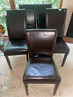 Front view of five brown faux leather Parsons chairs including four matching tall chairs and one shorter chair in front.