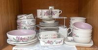 Front view of cabinet shelf showing assortment of Pfaltzgraff Cape May pattern dishes, mugs, and bowls stacked neatly with dish organizer.