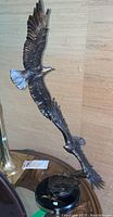 Full view of the metal eagle sculpture with two eagles soaring and artist signature visible on the base.