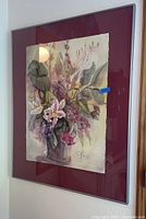 Frontal view of signed watercolor floral painting in maroon mat and silver frame