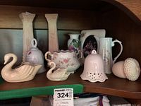 Shelf with decorative Lenox swan figurines, porcelain bell, acorn figure, floral sugar bowl missing lid, small floral pitcher, and candle holder.