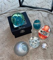 Top-down view showing all six glass paperweights including boxed green-blue signed piece