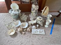 Photo showing full lot with shells, decorated bucket, glass jar filled with shells, conch lamp, shell painted footed mugs, shell bowls and decorative coral pieces spread on carpet.