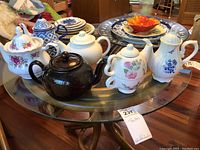 Tea pots arranged on glass tables showing different styles including floral prints, solid brown and blue and white porcelain.