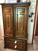Full front view of the wood armoire showing two large paneled doors with decorative handles and two bottom drawers.